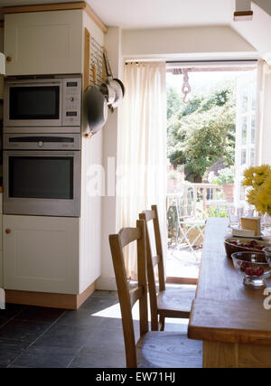 Semplici tavoli e sedie in legno nella sala da pranzo del cottage cucina con montato a parete doppia forni Foto Stock