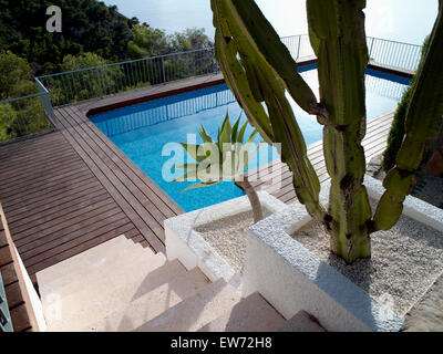 Tall cacti in letti di ghiaia accanto a gradini in pietra di turchese piscina su una collina che si affaccia sull'oceano Foto Stock