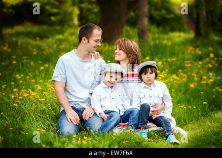 Famiglia di quattro, padre, madre e due ragazzi, genitore guardando ogni altro, ridendo, sorridente, avvolgente, dando un bacio, tenendo fl Foto Stock