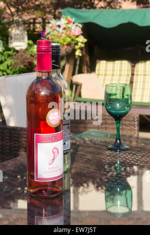 A piedi nudi white Zinfandel arrossire bottiglia di vino in confezione chiusa, su un tavolo da giardino nel Regno Unito. Foto Stock