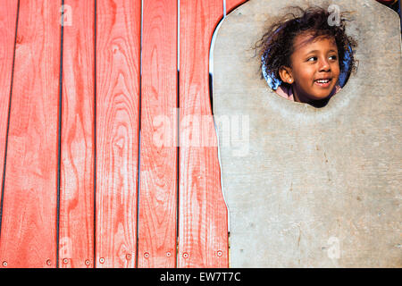 Ragazza sorridente prendendo la sua testa attraverso un foro nella parete, Perth, Australia Foto Stock