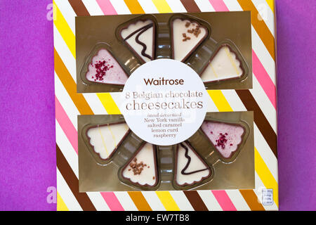 Scatola di Waitrose 8 cioccolato Belga cheesecake decorati a mano New York vaniglia, salati caramello, cagliata di limone e lampone impostato su sfondo viola Foto Stock