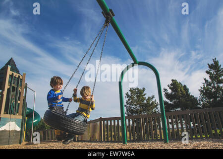 Due giovani ragazzi basculante in un pneumatico oscillare in un parco Foto Stock