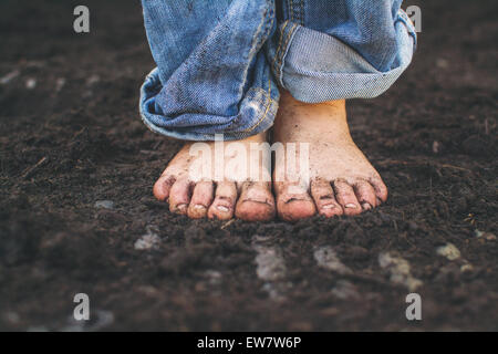 Primo piano dei piedi sporchi di un ragazzo che si trova nel terreno Foto Stock