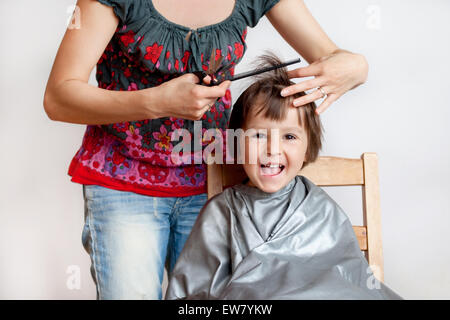 Carino piccolo ragazzo, avente taglio di capelli, sorridente felicemente, sfondo bianco Foto Stock