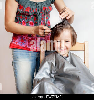 Carino piccolo ragazzo, avente taglio di capelli, sorridente felicemente, sfondo bianco Foto Stock