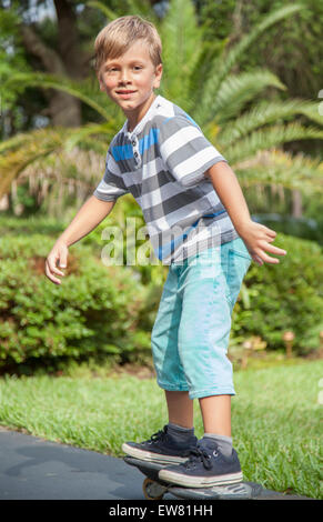 Giovani dai capelli biondi boy skateboarding in park Foto Stock