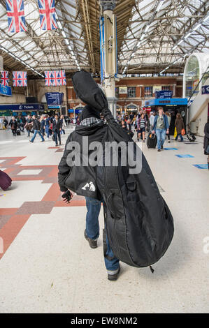 Un uomo su una strada di Londra che porta un contrabbasso in un sacchetto di protezione attraverso la stazione di Victoria a Londra Foto Stock