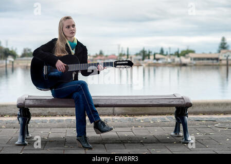 Bella ragazza bionda seduta sul banco di lavoro e a suonare la chitarra Foto Stock