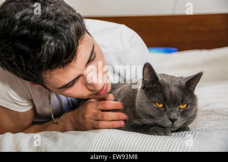 Bel giovane uomo Animal-Lover su un letto, avvolgente e coccole il suo grigio gatto domestico Pet. Foto Stock