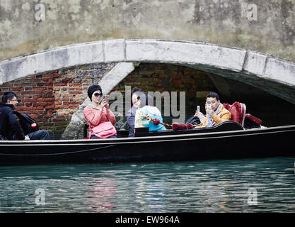 Turisti asiatici scattare fotografie su telefoni cellulari come loro gondola passa sotto un ponte Venezia Veneto Italia Europa Foto Stock