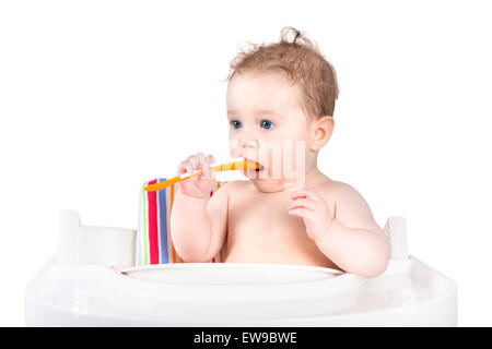 Funny little baby in una sedia alta tenendo un cucchiaio, isolato Foto Stock