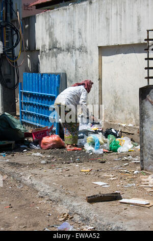 Una donna anziana è di lavaggio attraverso la plastica per materiale riciclabile su una strada di città in Kampong Cham, Cambogia. Foto Stock