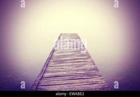 Vintage immagine filtrata del vecchio molo in legno nella fitta nebbia con forte effetto vignetta. Foto Stock