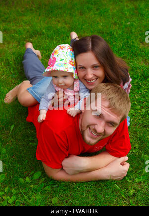 Felice giovane e bella famiglia sdraiati sull'erba verde. Foto Stock