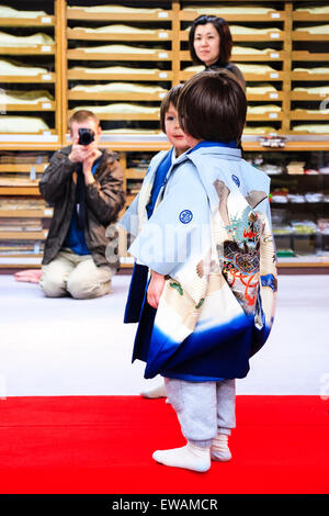 Razza mista, Japanese-English bambino, ragazzo, 5 anno di età, in piedi in ambienti interni in kimono tradizionali in posa mentre il padre si mette in ginocchio per scattare una foto Foto Stock