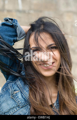 Ritratto di una giovane donna bruna all'esterno. La donna è sempre sorridente e ha capelli tousled Foto Stock