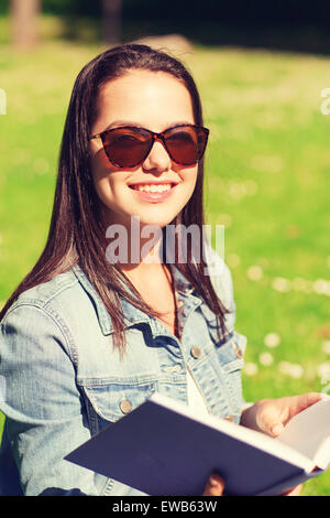 Sorridente ragazza giovane con libro seduti in posizione di parcheggio Foto Stock