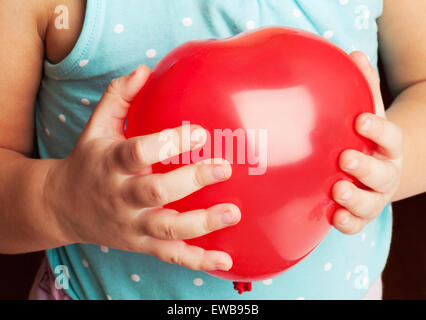 Caucasian Baby girl detiene il cuore rosso palloncino di forma nelle sue mani Foto Stock