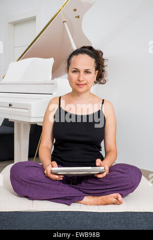 Donna nella sua anni trenta in abiti casual lavora da casa sul suo tablet Foto Stock