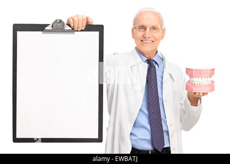 Studio shot di una matura dentista tenendo una dentiera e una clipboard con una carta vergine su di esso isolato su sfondo bianco Foto Stock
