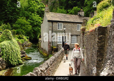 Dog walkers passano dalla pietra costruito case su acqua Peakshole nel cuore di Castleton village, Peak District DERBYSHIRE REGNO UNITO GB UE Foto Stock