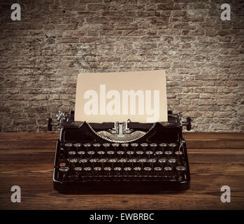 Macchina da scrivere retrò poste su assi di legno. Il vecchio muro di mattoni come sfondo con copyspace. Foto Stock