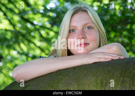 Bionda caucasica ragazza adolescente appoggiata sul ramo di albero in natura Foto Stock