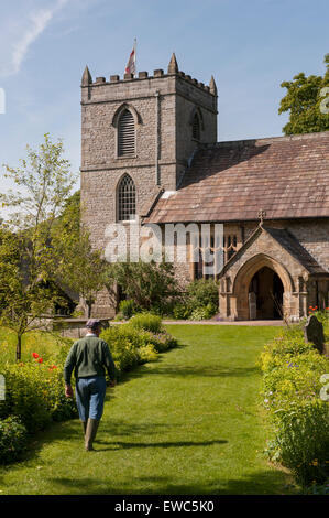 La chiesa di Santa Maria, Kettlewell, Yorkshire Dales, Inghilterra, Regno Unito. Vista del giardiniere sul percorso nel bellissimo giardino con fiori di prato, estate sole e cielo blu. Foto Stock