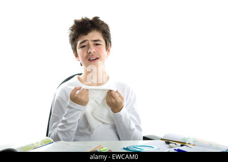 Carino liscia caucasico-pelato boy tristemente seduto di fronte a compiti che indossa una bianca maniche lunghe t-shirt e azienda hankerchief per asciugare le lacrime Foto Stock