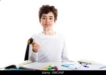 Adolescente caucasica ragazzo squillo di seduta di un piccolo campanile con la mano destra mentre si fanno i compiti Foto Stock