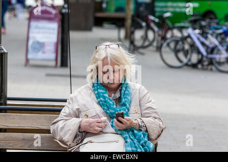 Persone di mezza età bionda donna seduta su un banco di controllo il suo telefono cellulare per i messaggi. Foto Stock