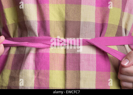 Una donna legatura di una rosa e giallo plaid grembiule. Foto Stock