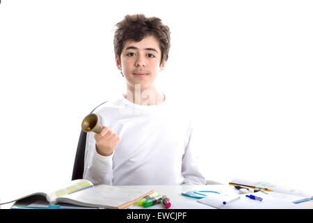 Liscia caucasico-pelato ragazzo squillo di seduta di un piccolo campanile con la mano destra mentre si fanno i compiti Foto Stock