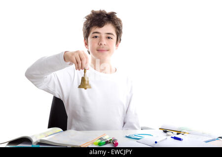 Liscia caucasico-pelato ragazzo squillo di seduta di un piccolo campanile con la mano destra mentre si fanno i compiti Foto Stock