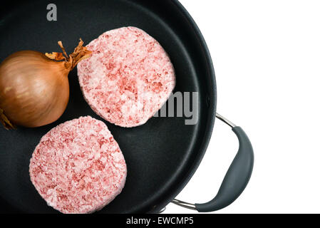 Una cipolla fresca e due beefburgers congelati in una padella nera su sfondo bianco con copyspace Foto Stock