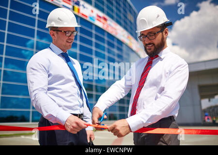 Architetto felice il taglio di un nastro rosso al di fuori con il suo collaboratore nelle vicinanze Foto Stock