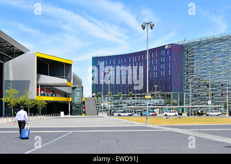 Business uomo a camminare verso la sala delle esposizioni ingresso orientale di Londra Excel edificio giallo & adiacente Aloft W hotel in East London Docklands REGNO UNITO Foto Stock