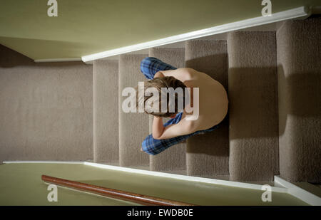 Un bambino seduto sulle scale con la testa tra le mani cercando sconvolto Foto Stock