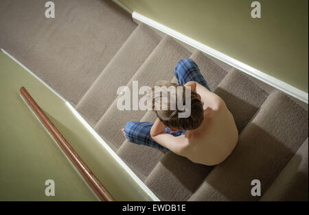 Un bambino seduto sulle scale con la testa tra le mani cercando sconvolto Foto Stock
