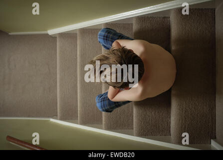 Un bambino seduto sulle scale con la testa tra le mani cercando sconvolto Foto Stock