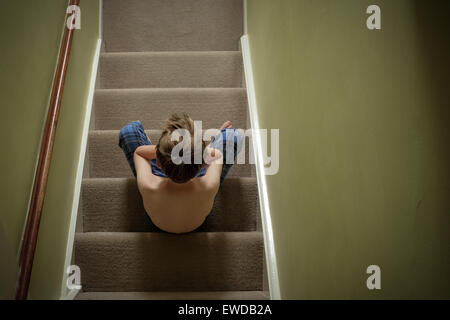 Un bambino seduto sulle scale con la testa tra le mani cercando sconvolto Foto Stock