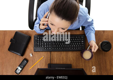 Donna che lavorano presso la sua scrivania sul suo telefono cellulare parlando con qualcuno di tiro da birds eye vista guardando verso il basso Foto Stock