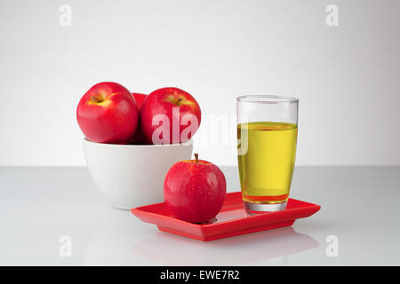 Le mele rosse e il succo in un recipiente e su una targhetta sulla superficie riflettente. Foto Stock