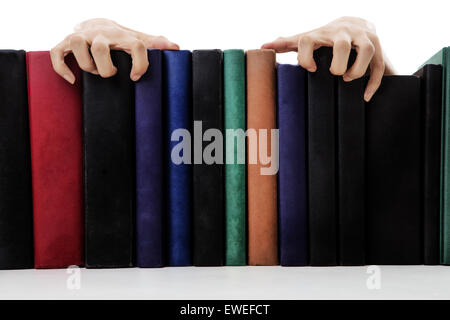 Creepy mani proveniente da sopra i libri su uno scaffale Foto Stock