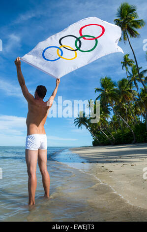 BAHIA, Brasile - MARZO 18, 2015: atleta sorge su rustico spiaggia brasiliana holding bandiera olimpica nel vento. Foto Stock