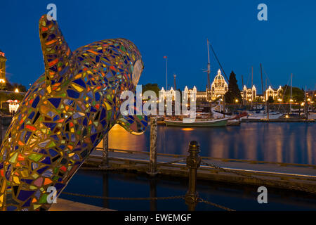 Victoria's Inner Harbour accesa al crepuscolo con il BC agli edifici del parlamento in background e un orca artistico in f Foto Stock