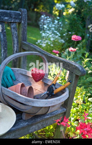Rustico sedia da giardino nel giardino soleggiato con tradizionale trug accessori per il giardinaggio e cuore decorazione emblema "l'amore" di giardinaggio Foto Stock