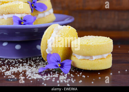 Pila di tradizionale stile Australiano yo-yo biscuit cookie sul viola polka dot stand decorato con fiori viola sul legno scuro Foto Stock