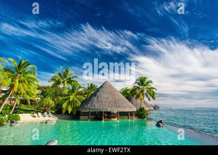 Piscina Infinity con spiaggia artificiale con palme e bar accanto all'oceano tropicale Foto Stock